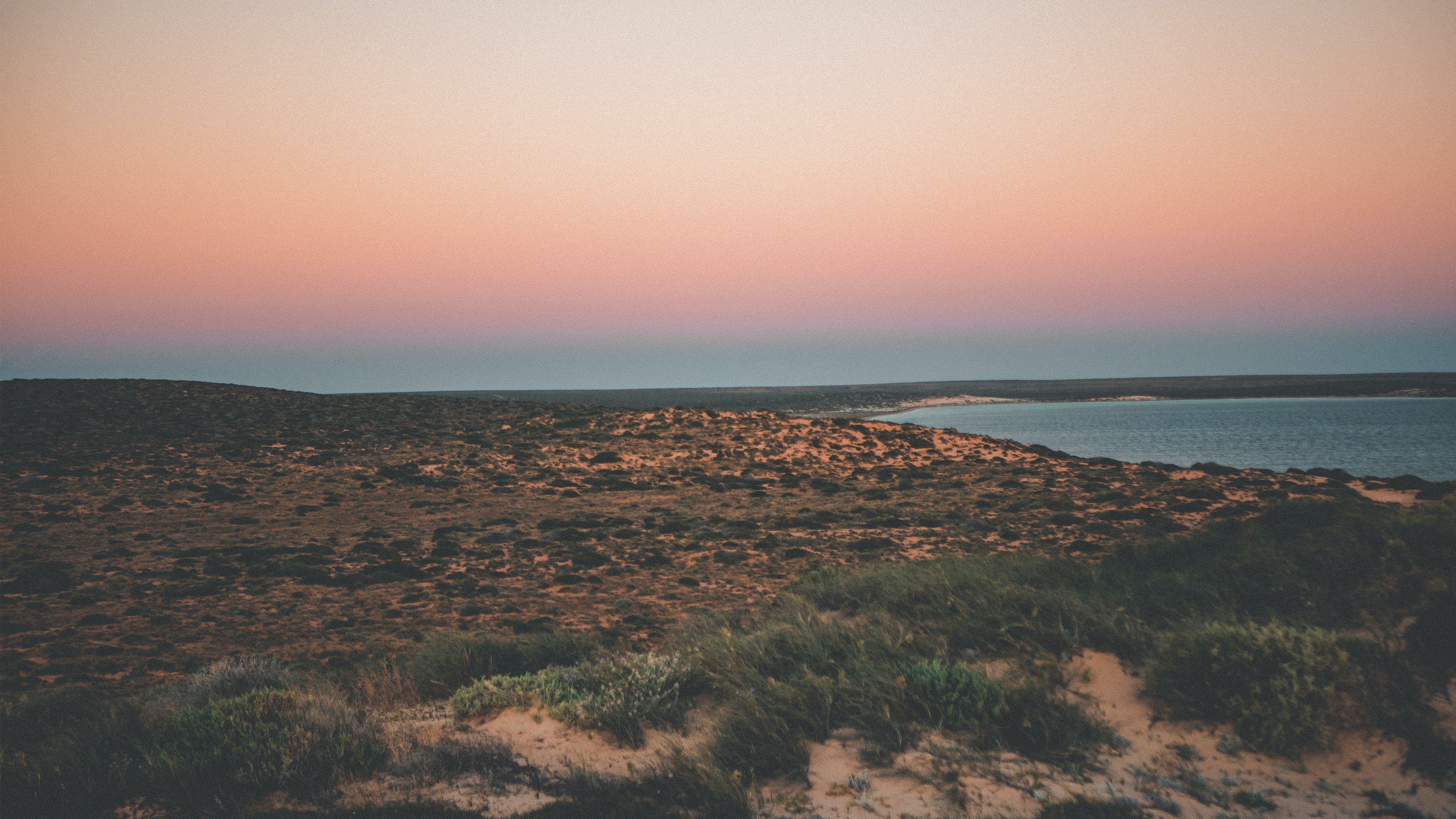 Sonnenuntergang in Shark Bay, West Australien. Man sieht eine raue Küstenlandschaft und eine Bucht mit klarem Wasser.