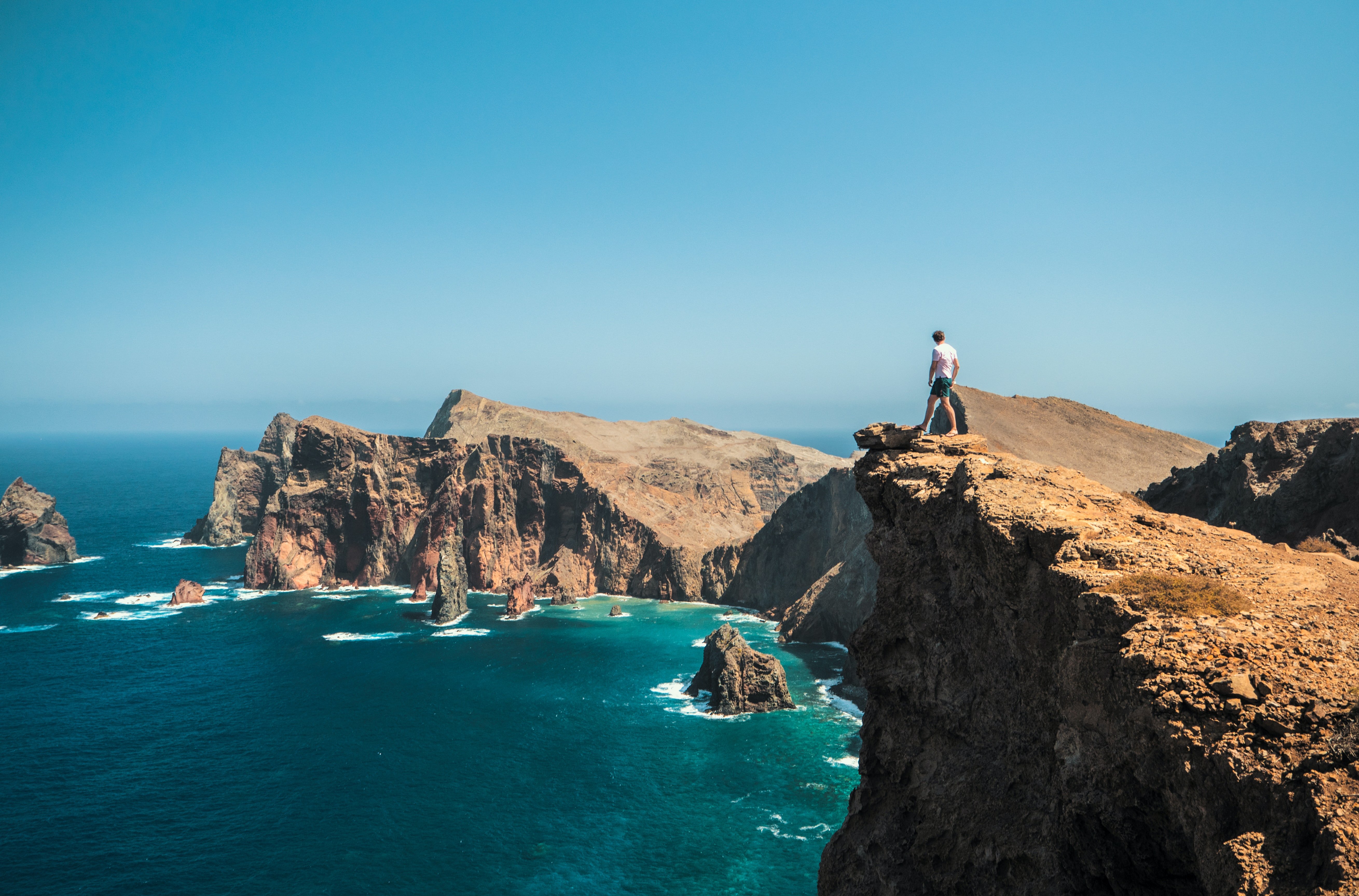 A hiker stands on a cliff above the blue Atlantic Ocean.