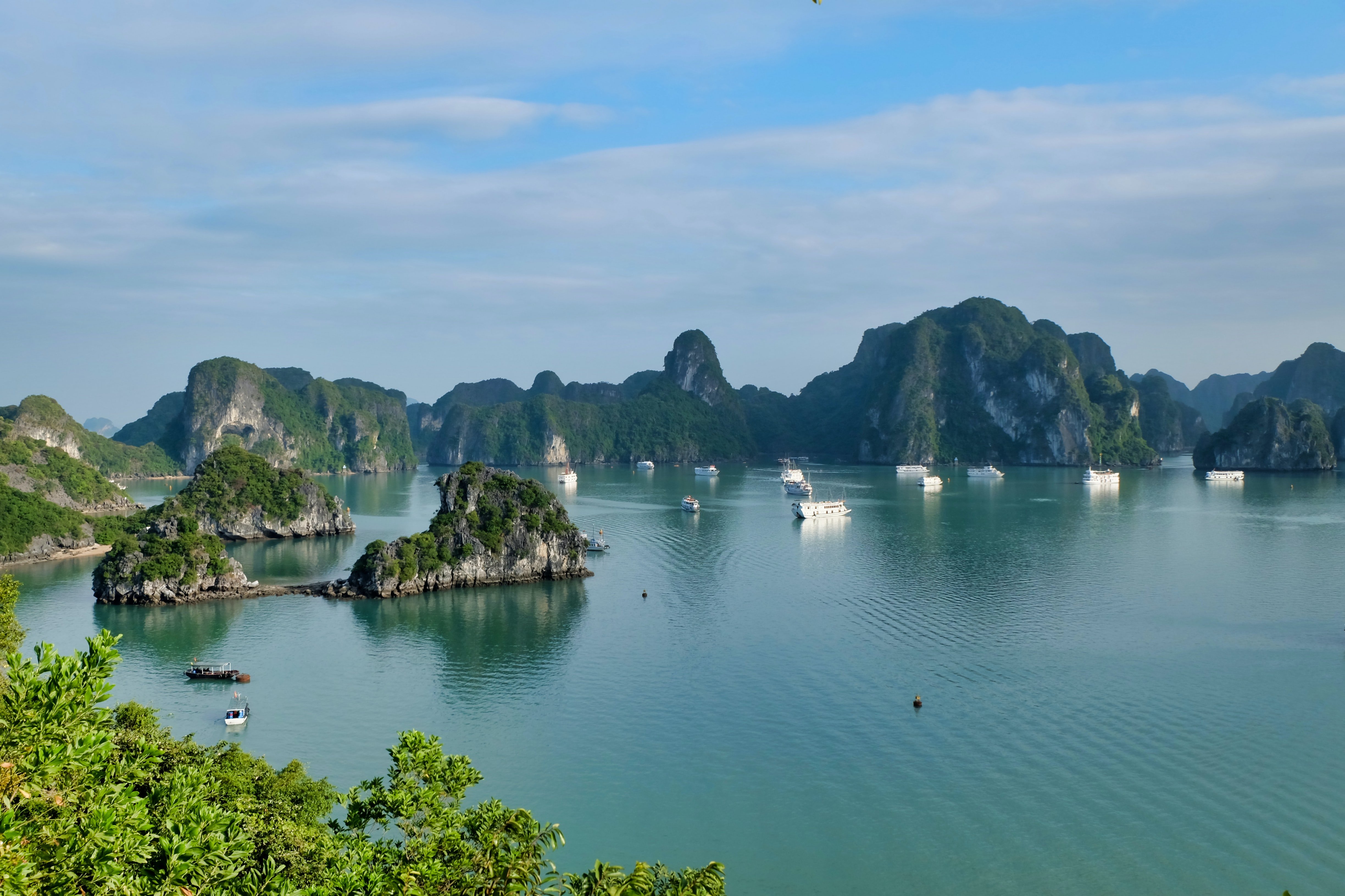 A view of Halong Bay, Vietnam with ships in the blue water and high cliffs.