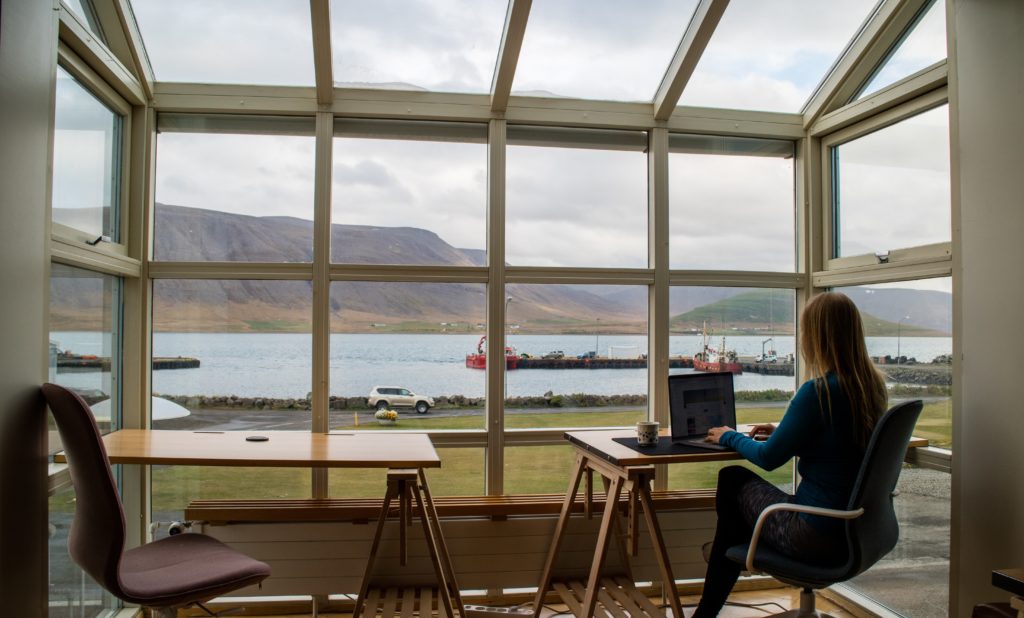 a woman sat with a laptop looking out on to a lake and mountain for remote work in winter