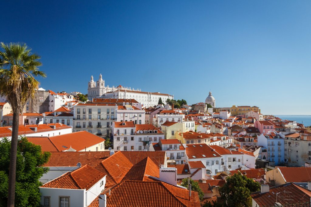 a view of Lisbon, Portugal in the day time, all with orang roofs and painted white walls.