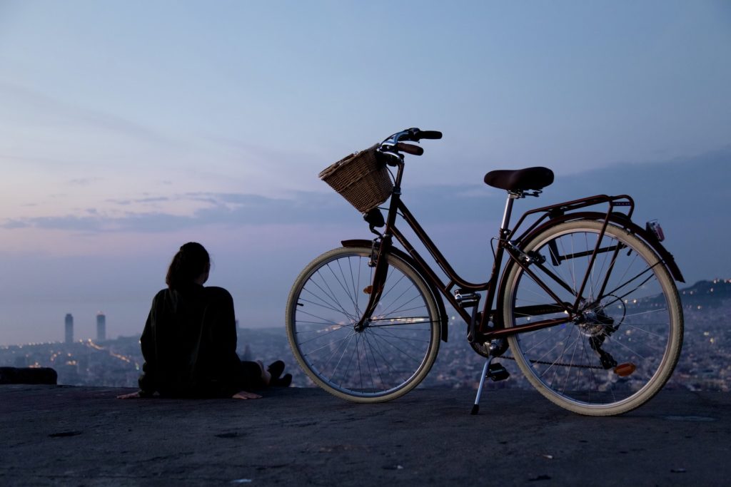 a person sitting on a cliff edge looking over an amazing city view with a bike next to them
