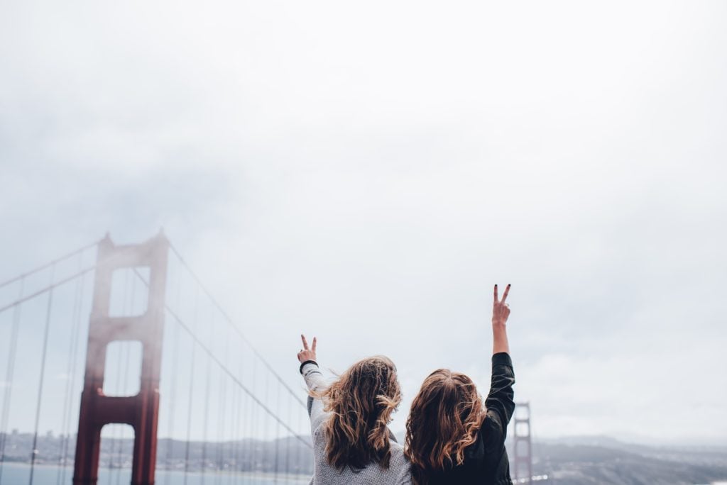 zwei Mädchen die vor der Brücke in San Francisco, USA, stehen. Beide zeigen ein peace Zeichen in die Luft