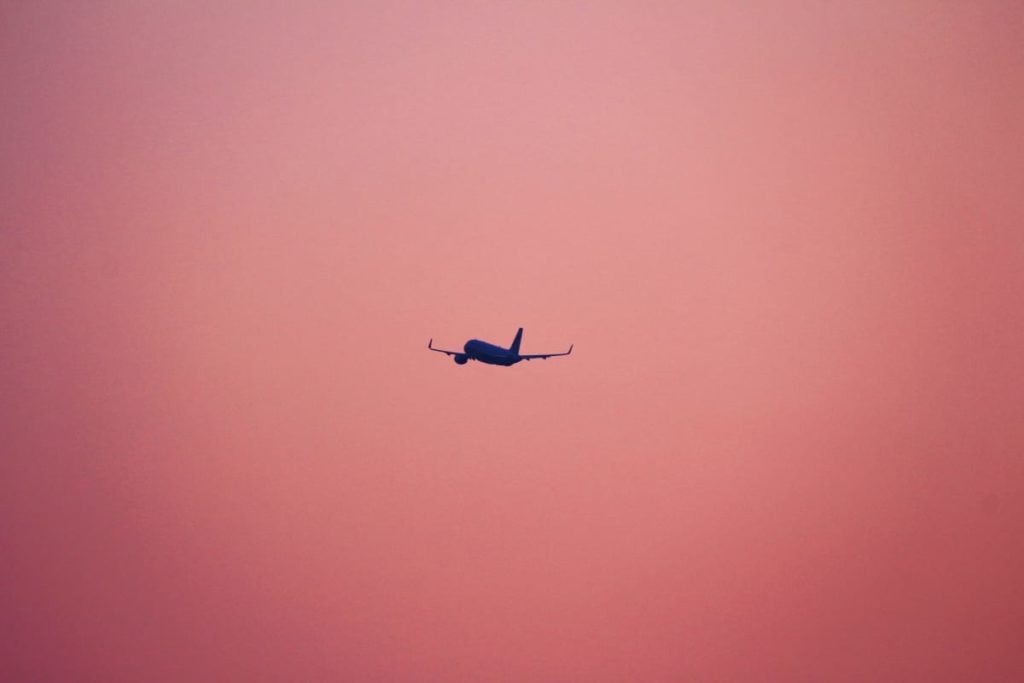 a plane flying in the pink sky perfect last minute travel tip