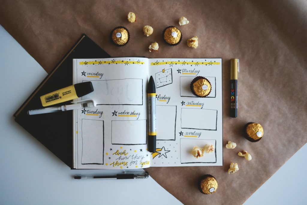 a note pad with drawings of a daily plan with pens and highliters and chocolate.