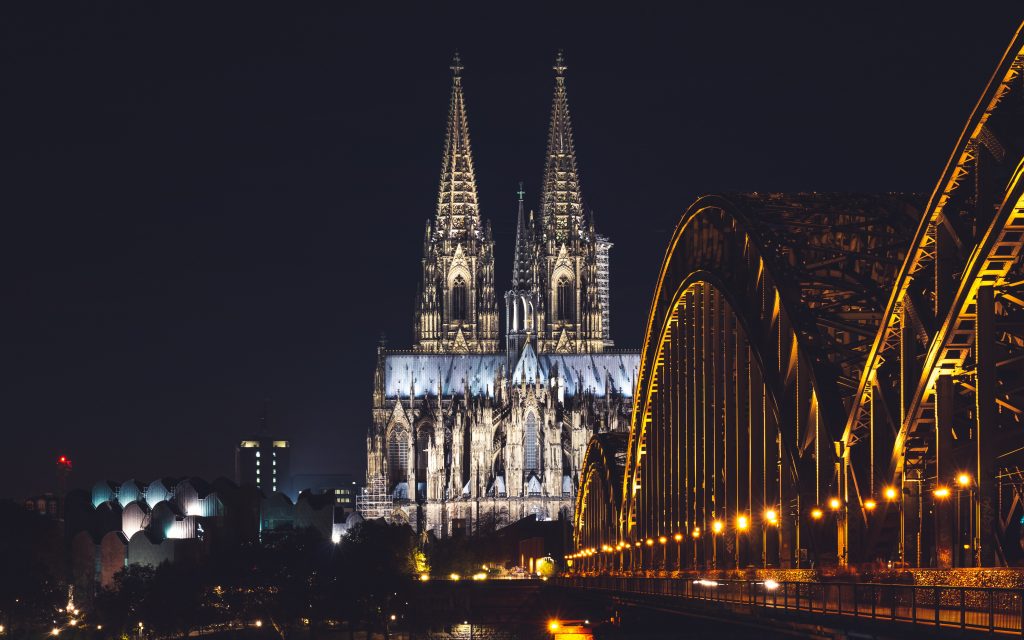 A view of cologne in the evening with the bridge lit up and church in the background.