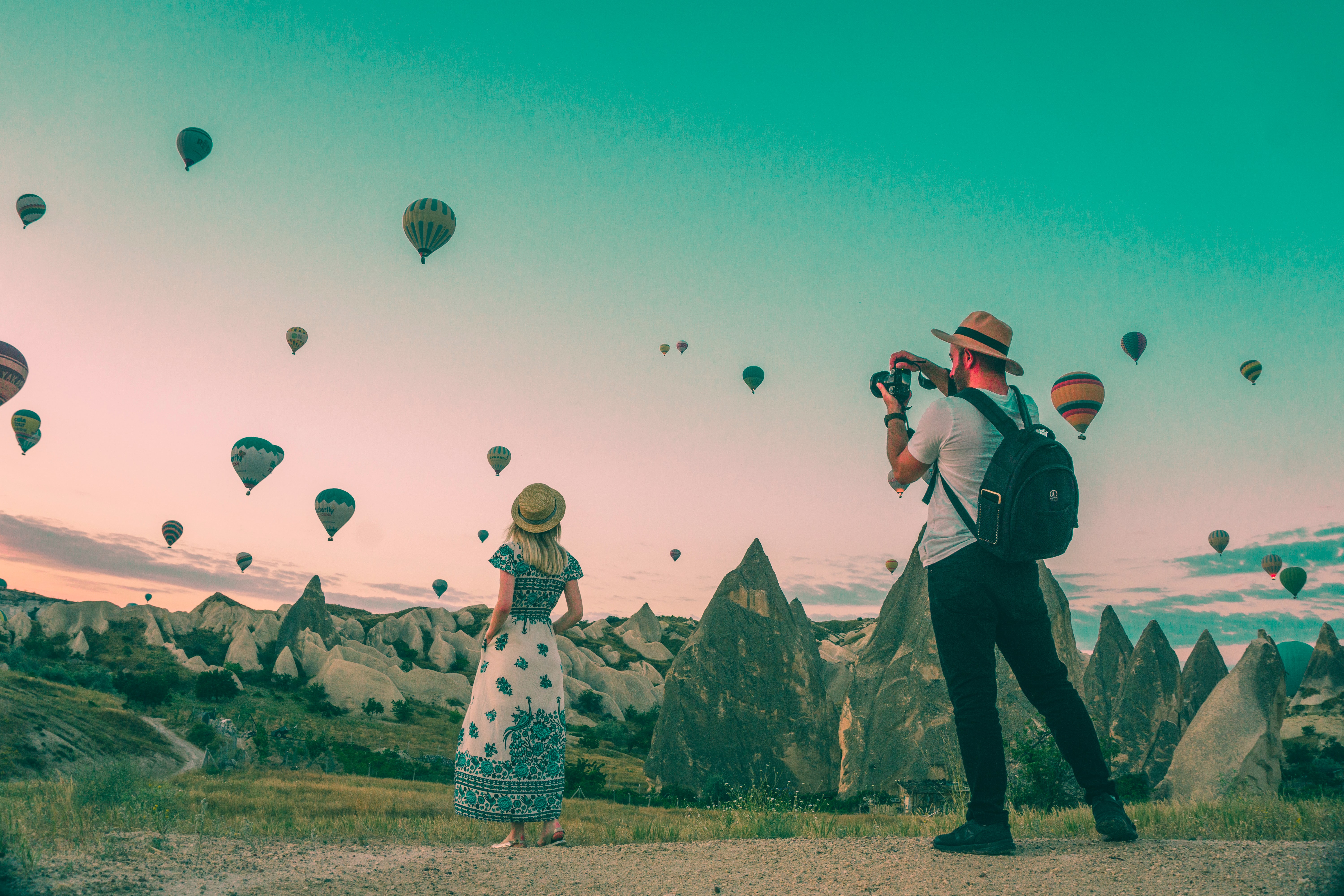 Two people taking pictures surrounded by rock structures and hot air balloons travel words
