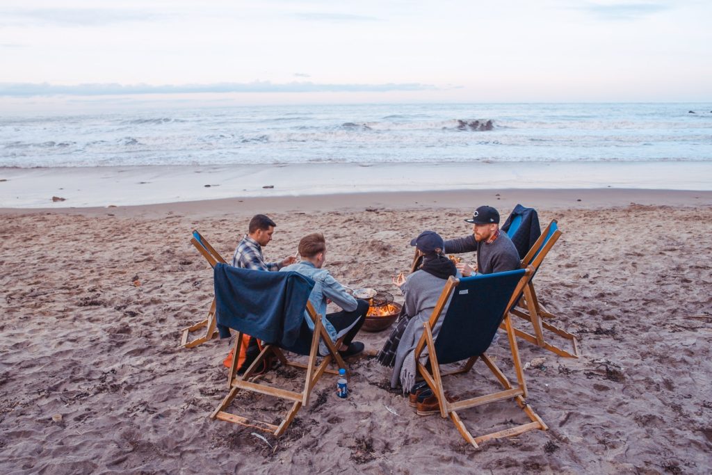 friends together and sitting on a beautiful beach around a campfire while chatting 