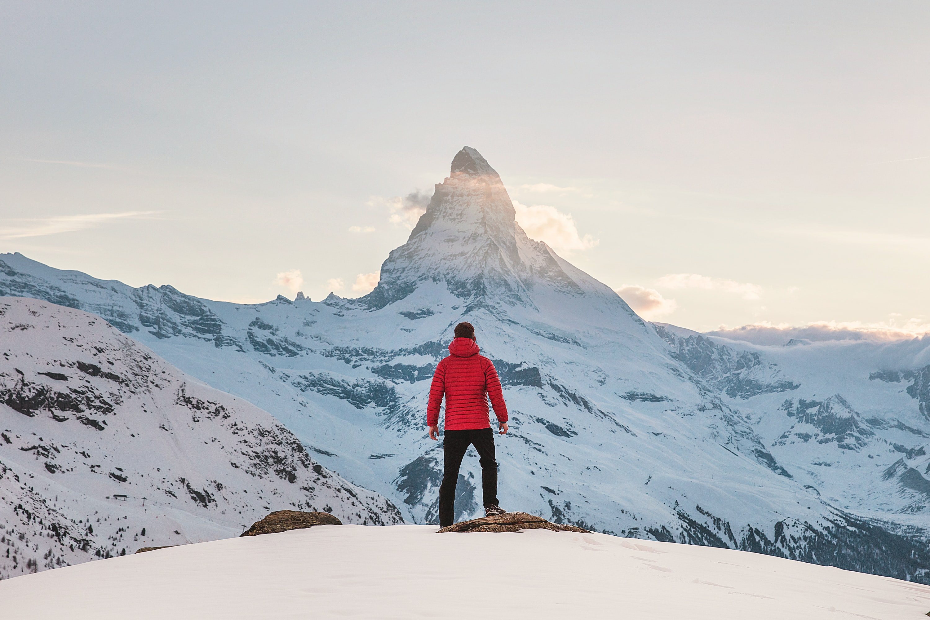 Ein Wanderer in roter Jacke vor dem verschneiten Matterhorn in Zermatt, wo man wunderbar klettern kann.