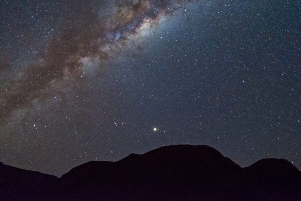Klarer Sternenhimmel über schwarzen Bergen mit Milchstraße in Südafrika.