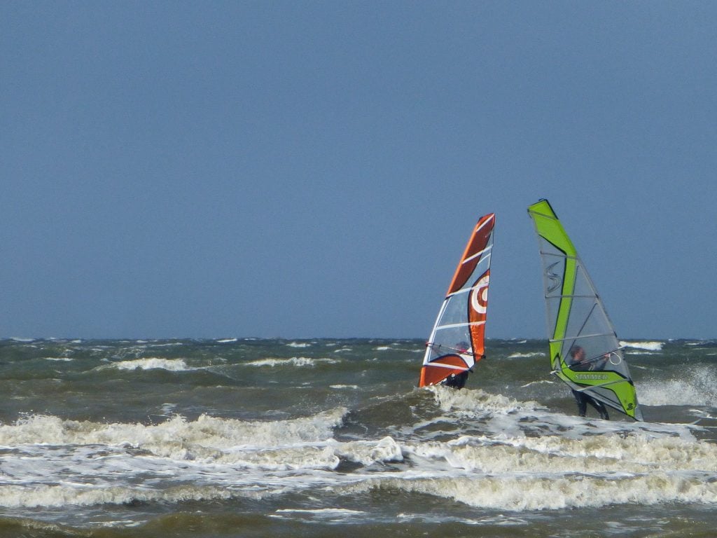 Zwei Windsurfer auf den rauen Wellen vor St. Peter-Ording unter blauem Himmel 