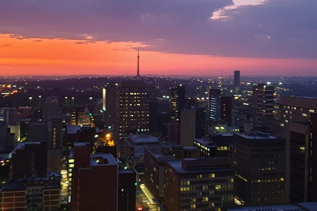 Sonnenuntergang über Johannesburg mit Himmel in orange und lila und vielen Hochhäusern.