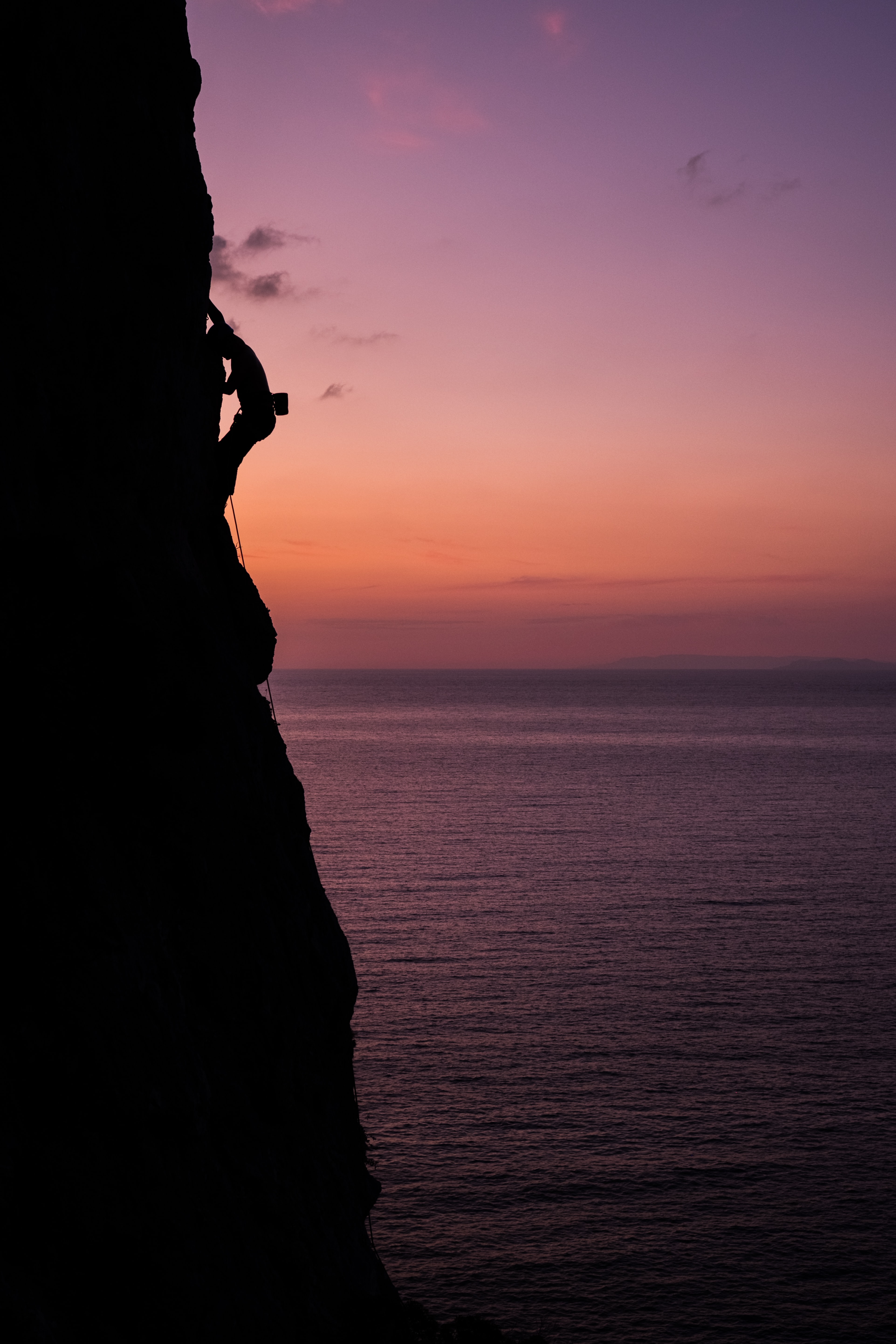 Kletterer an einer Klippe über dem Mittelmeer im Sonnenuntergang.