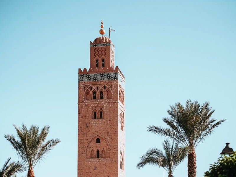 Ein hoher Turm in Marrakesh, Verziert mit bunten Fliesen im arabischen Stil, umringt von Palmen. Marrakesh ist ein Top Tipp für einen Städte-Trip