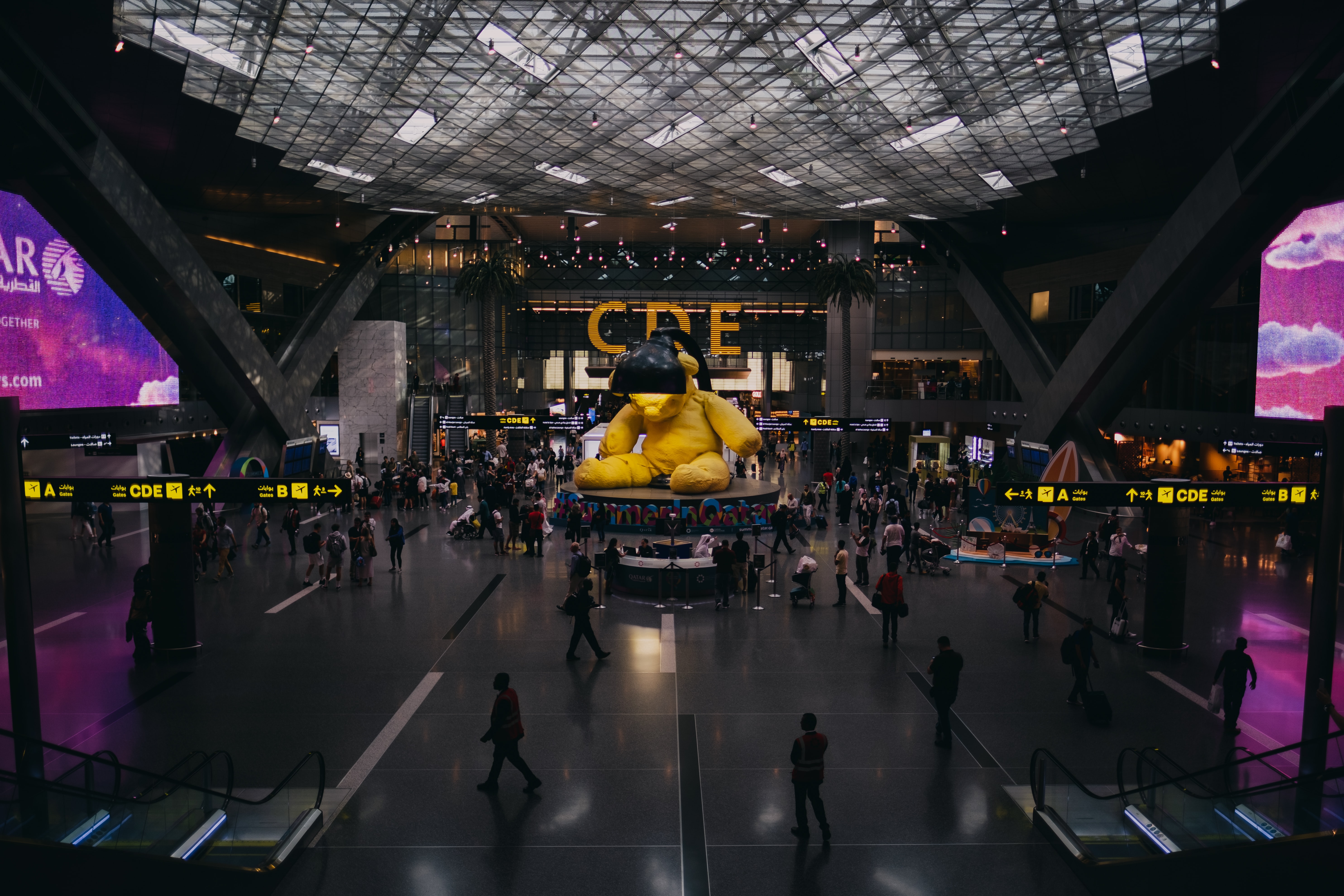 The main hall of Qatar airport bustling with people with a artwork in the middle