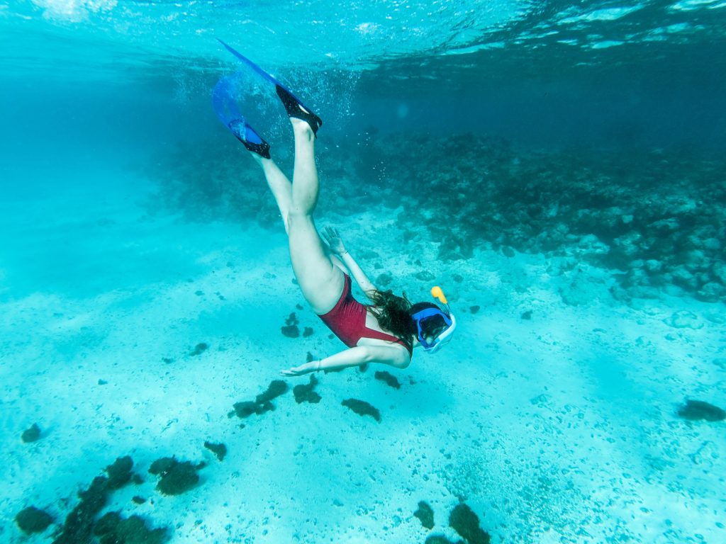 Woman diving in clear blue ocean water reaching the sea floor