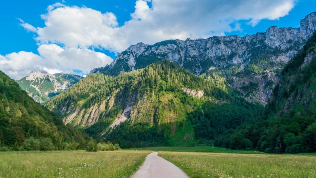 A pathway surrounded by greenrery and Austrian mountains, where Austria is one of the top alpine hiking trails