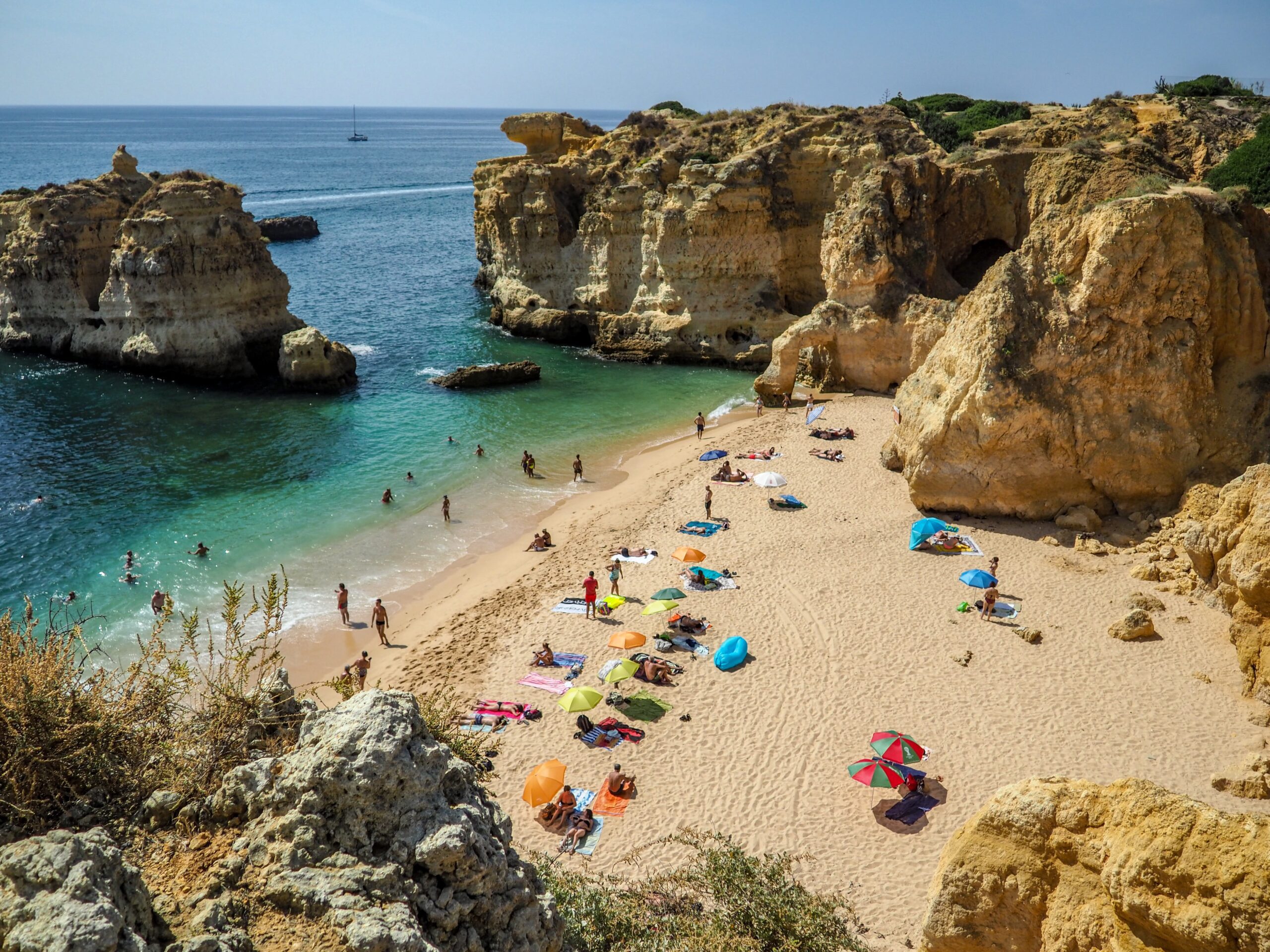 Die Algarve ist ein wunderschönes Reiseziel im August. Auf diesem Bild sieht man eine Bucht mit einem wunderschönen Sandstrand und bunten Sonnenschirmen. 